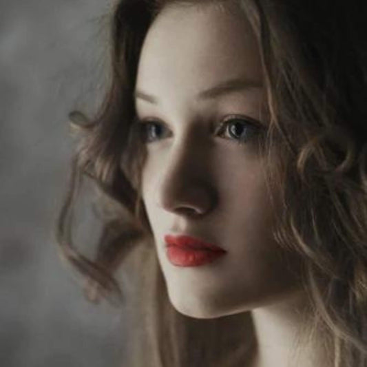 Ein Mädchen, dass nur die Lippen rot geschminkt hat. Sie trägt Locken und schaut verträumt.