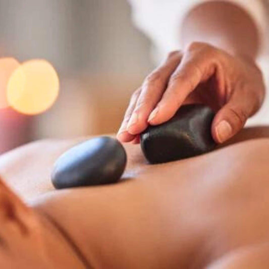 Ein Mann lässt sich mit einer "Hot-Stone-Massage" verwöhnen. Man sieht wie die Steine auf ihn gelegt werden.